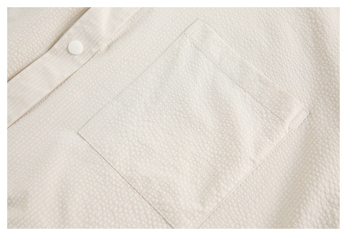 Close-up of an off-white textured garment with a square patch pocket and a white snap button.