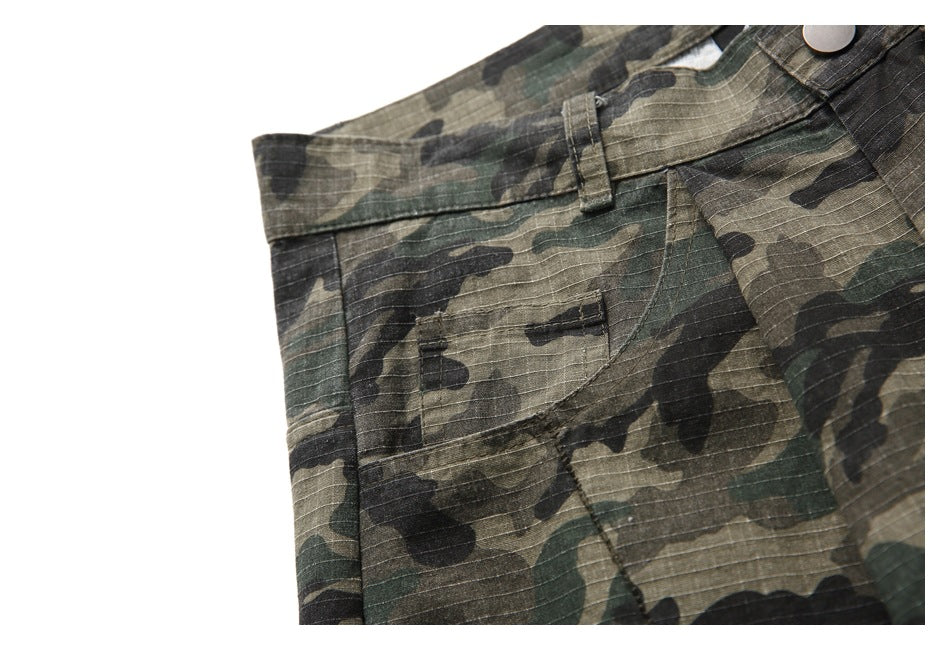 Close-up of olive, brown and black camouflage trousers showing the waistband, button and pocket stitching.