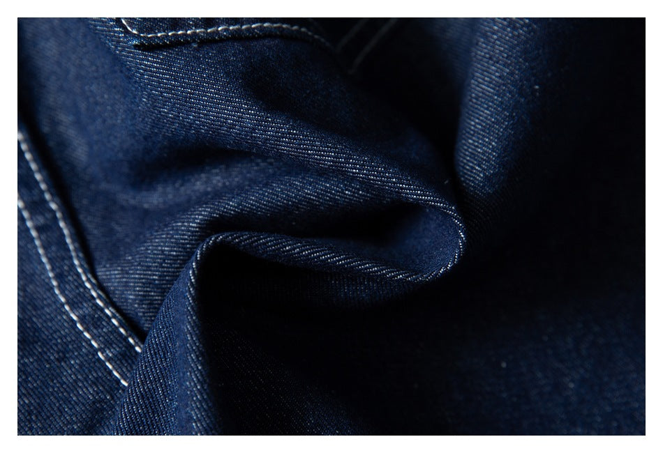 Close-up of dark indigo denim fabric folded to show its diagonal weave and contrast stitching.