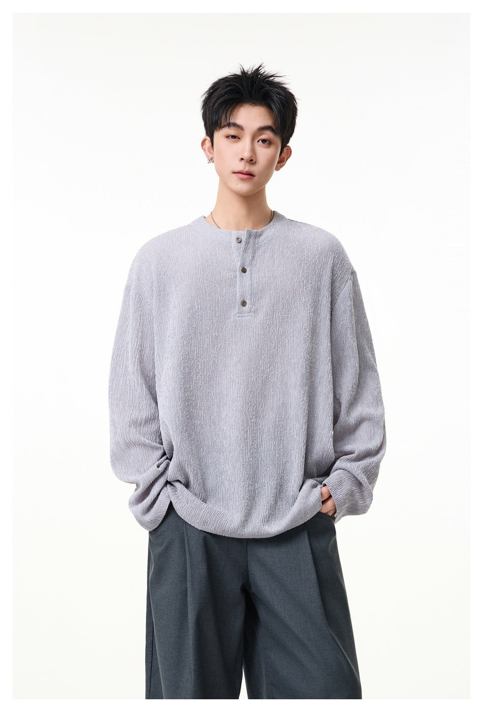 Model facing forward in a light gray oversized henley with a short button placket and dark trousers.