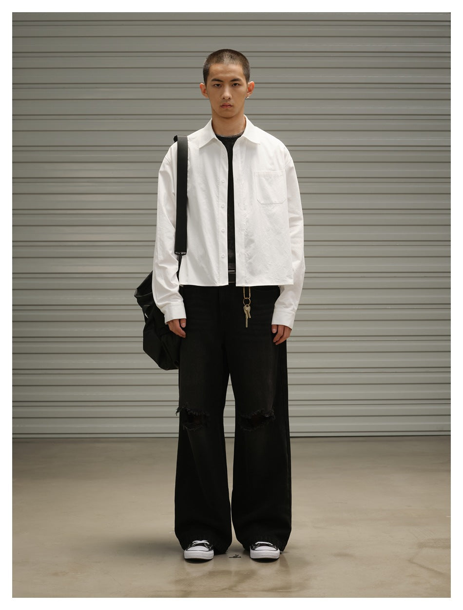 Model wearing a white cropped button-up shirt open over a dark tee with black wide-leg ripped jeans, full-length view