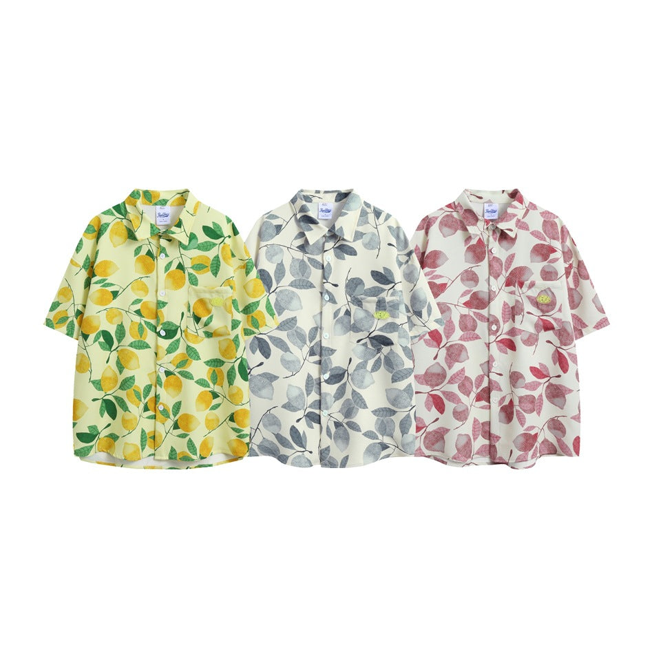 Three short-sleeve button-up shirts displayed side by side in yellow lemon, gray leaf, and pink leaf prints.