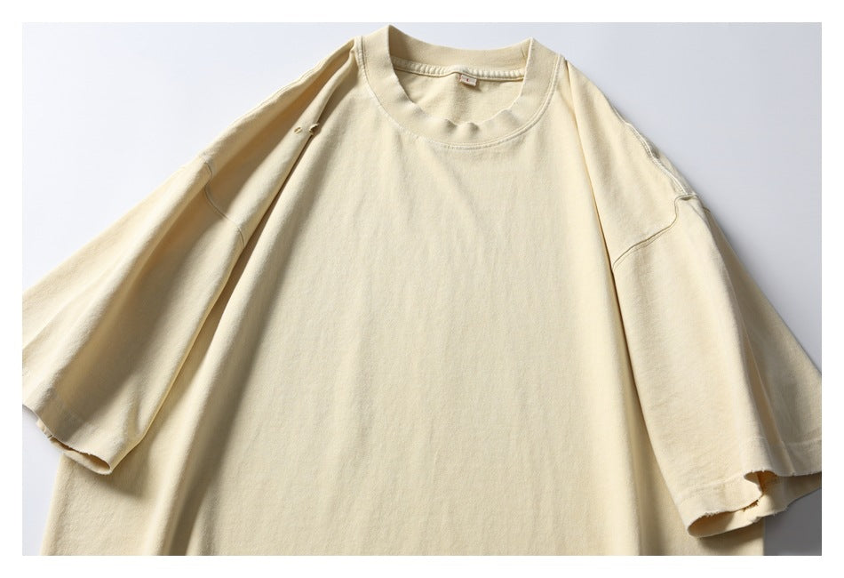 Flat-lay front view of a pale cream oversized short-sleeve crew-neck T-shirt with subtle distressed holes.