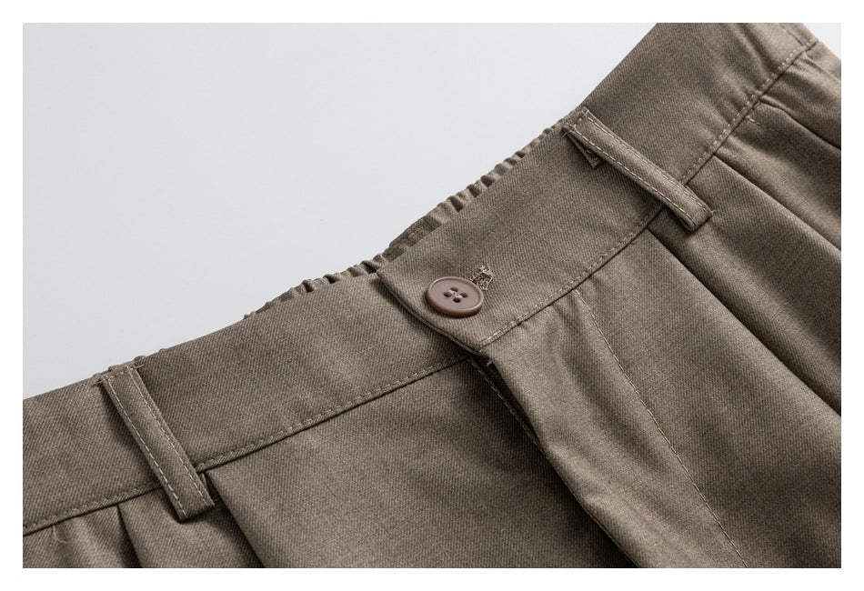 Close-up of taupe-brown trousers showing the buttoned waistband, belt loops and front pleats.