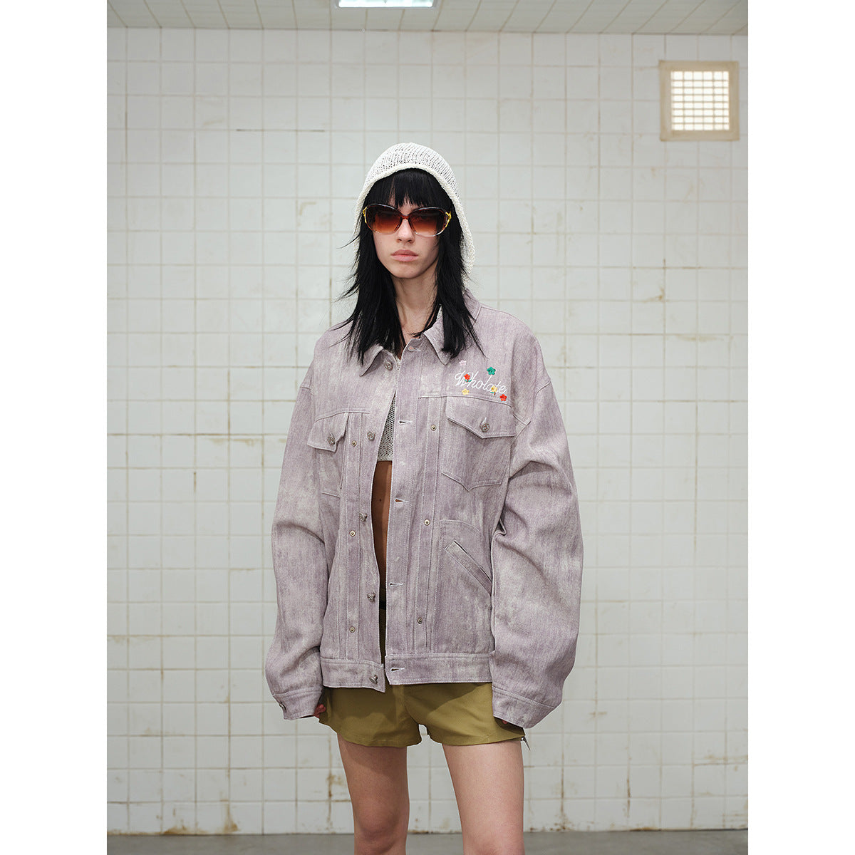 Closer front view of a model in a dusty mauve button-front jacket with flap pockets and floral chest embroidery.