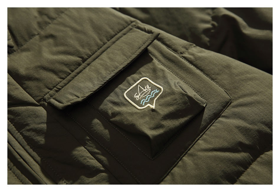 Close-up of an olive green jacket's flap pocket with a small embroidered emblem.