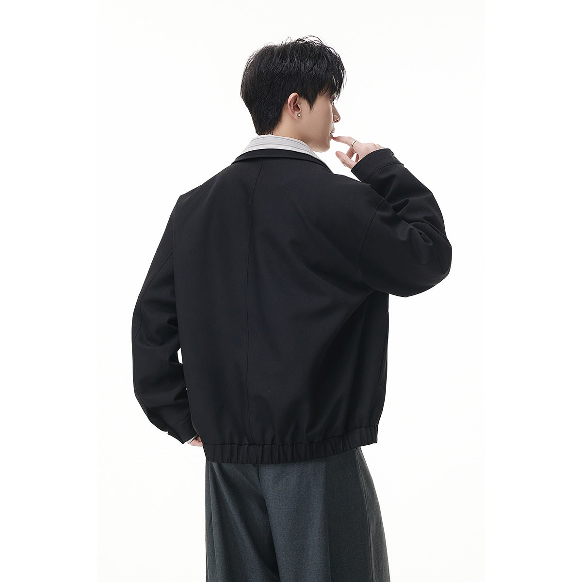 Rear view of a model wearing a relaxed black jacket with a gathered hem and wide collar.