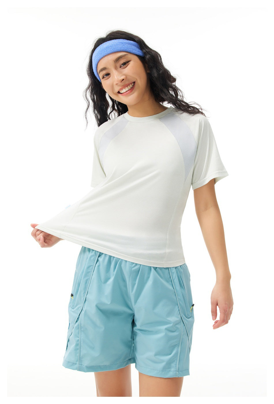 Close view of a model wearing a white color-block T-shirt and turquoise shorts, stretching the shirt hem.