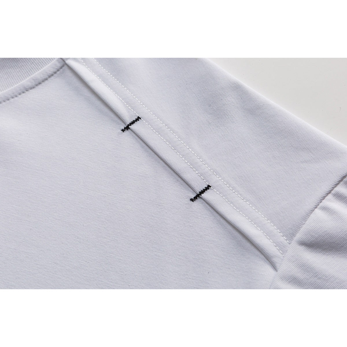 Close-up of a white T-shirt shoulder seam with two short black reinforcement stitches.