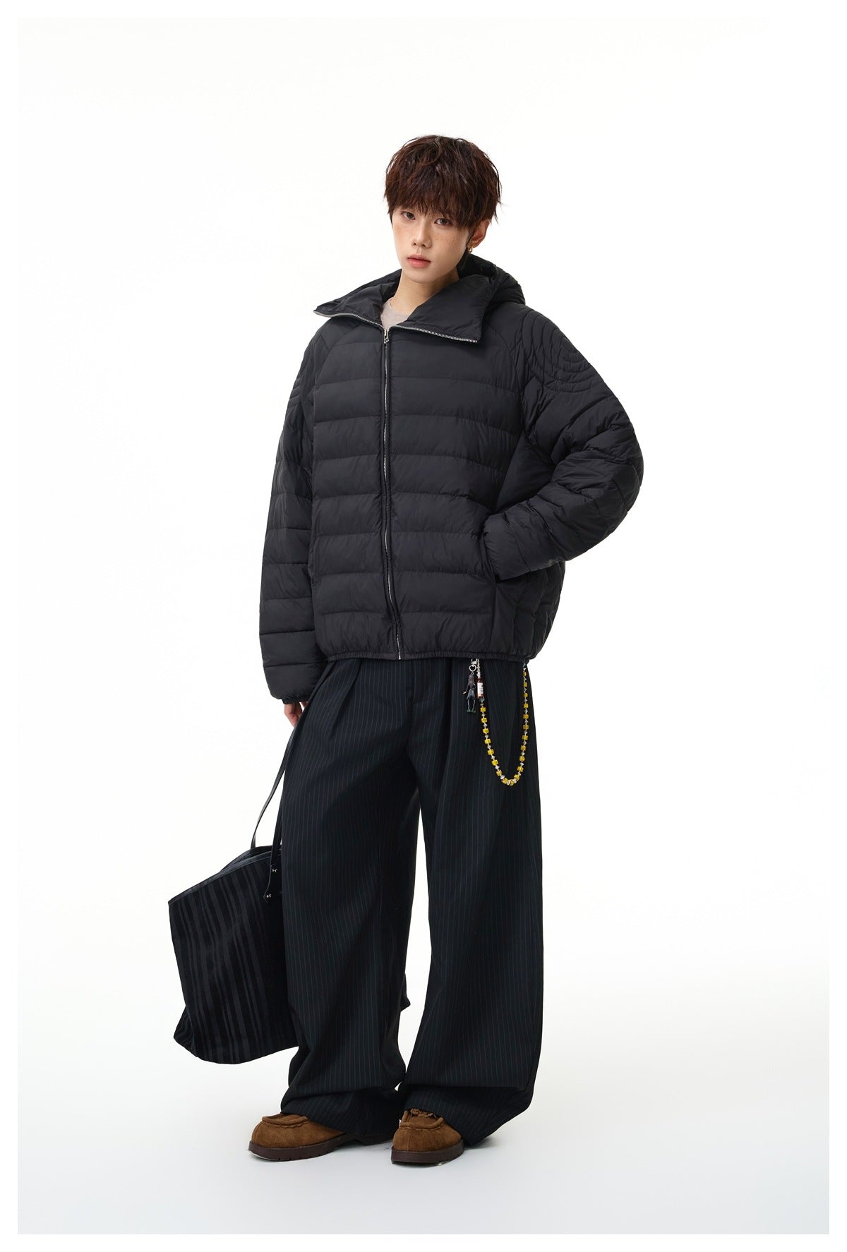 Model wearing a black quilted puffer jacket with a wide collar, styled with striped trousers and brown shoes.