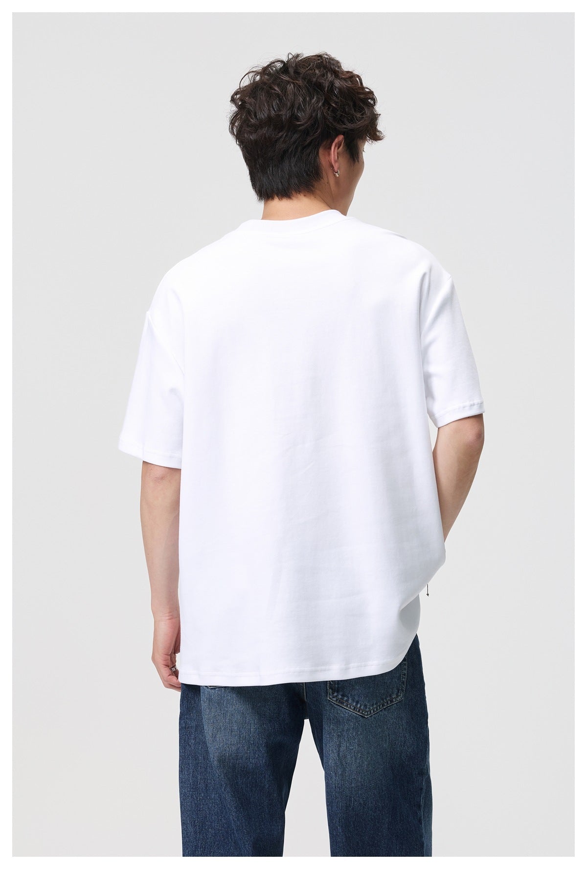 Back view of a model wearing an oversized plain white short-sleeve T-shirt with dark blue jeans.