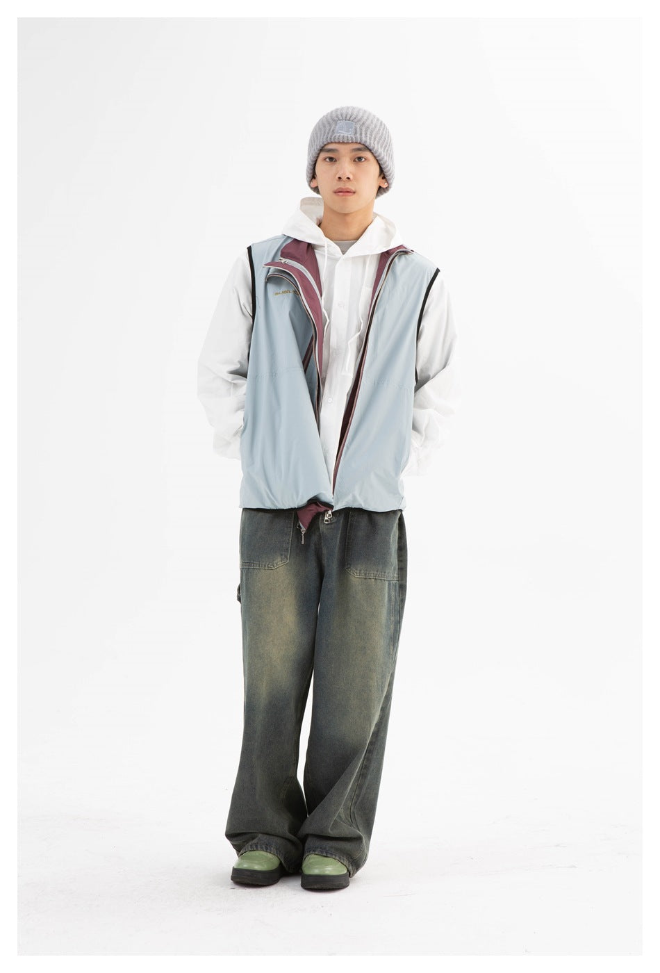Front view of a model wearing a pale blue and burgundy zip vest over a white hoodie and shirt, with dark wide-leg jeans.