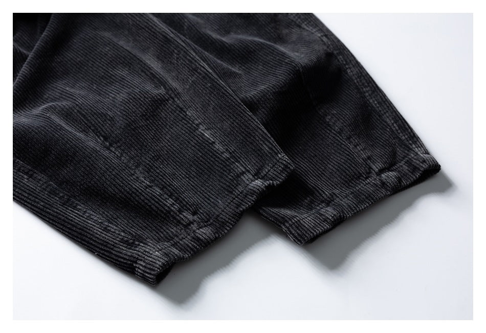 Close-up of black ribbed corduroy fabric with a stitched hem against a white background.