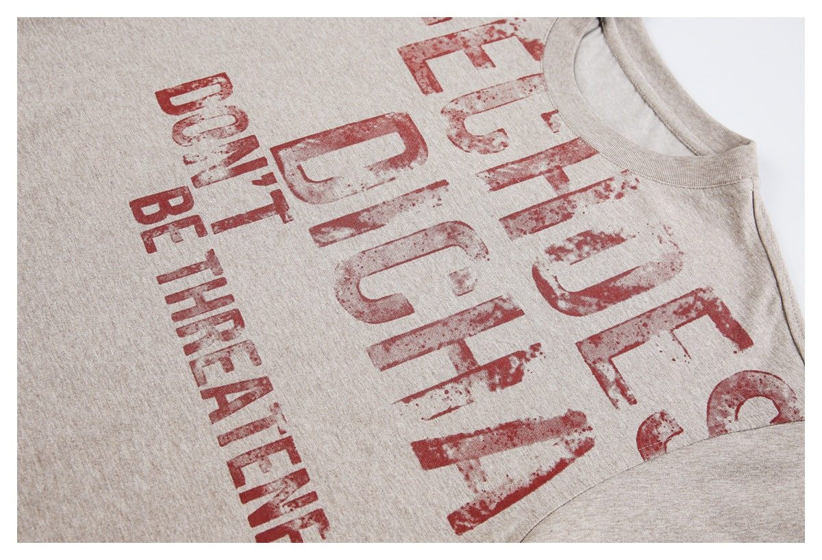 Angled close-up of a beige T-shirt front with large distressed red English lettering.