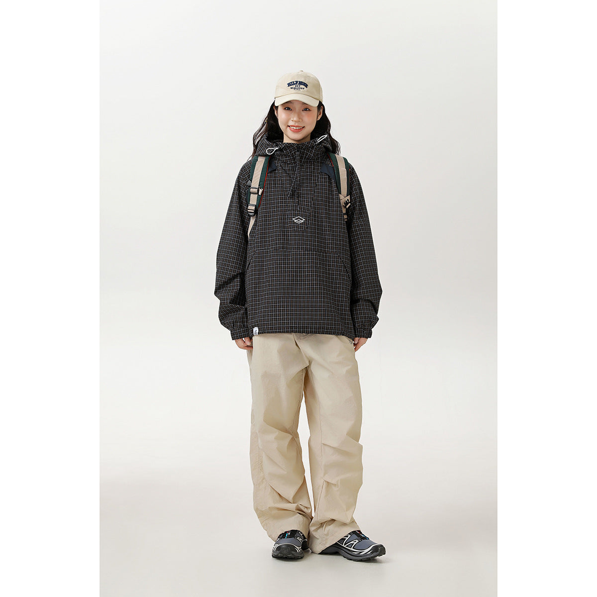Woman wearing a black checked hooded pullover jacket with a front pocket and drawstrings, paired with beige trousers.