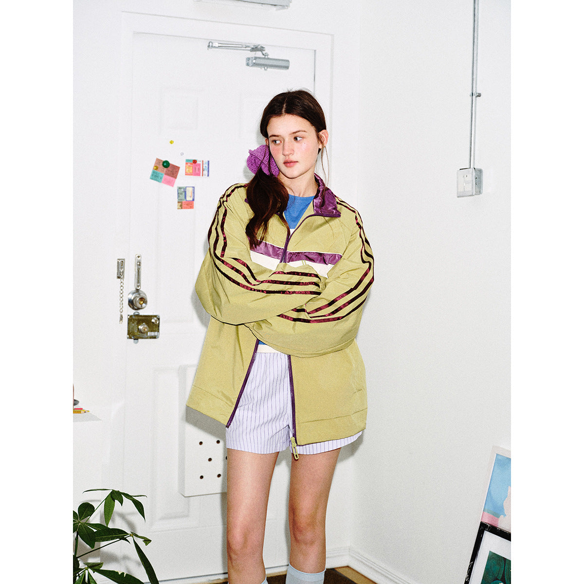 Closer view of a model in a khaki zip-up track jacket with purple-and-white chest stripes and striped sleeves.