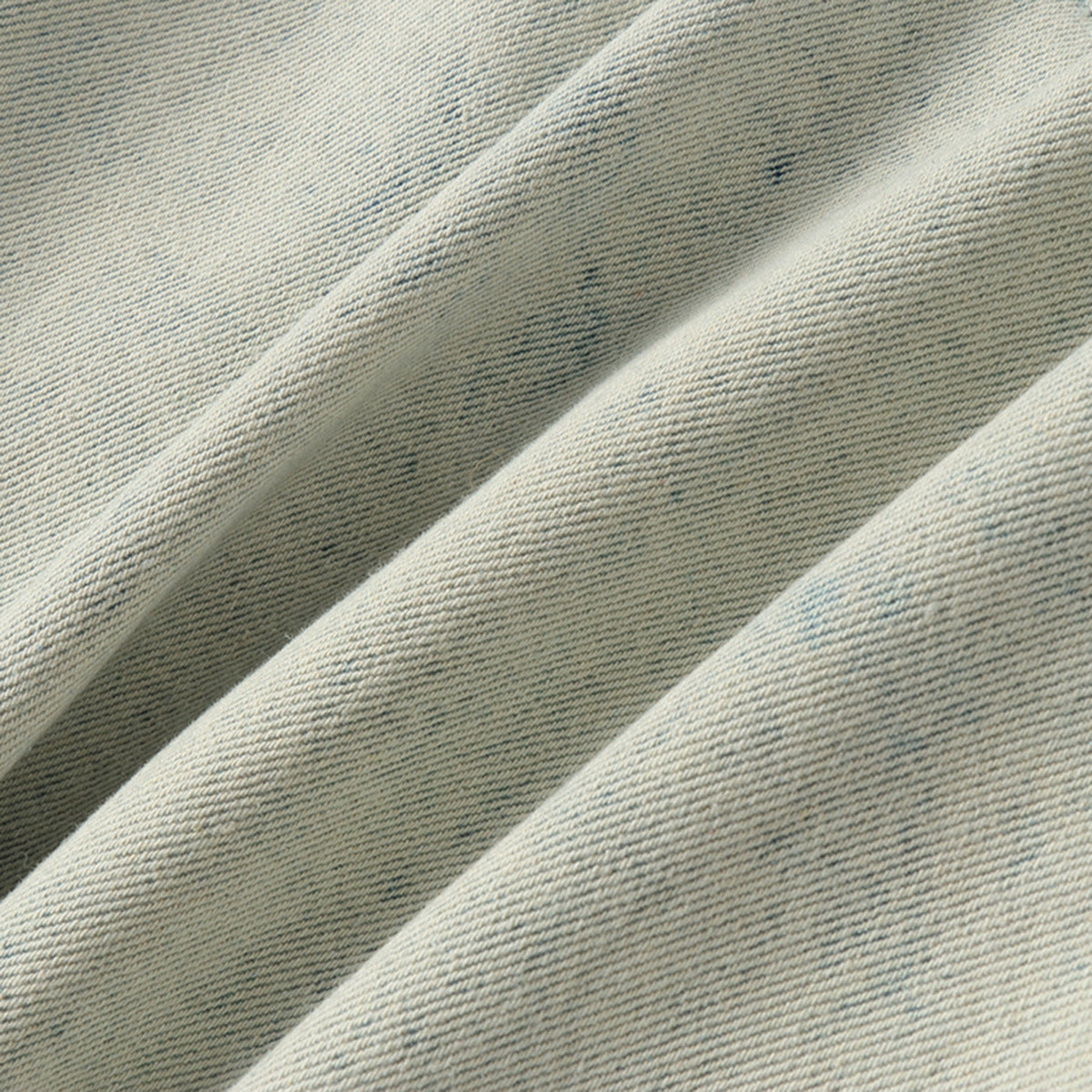 Macro view of the pale blue denim's diagonal weave and subtle washed markings.