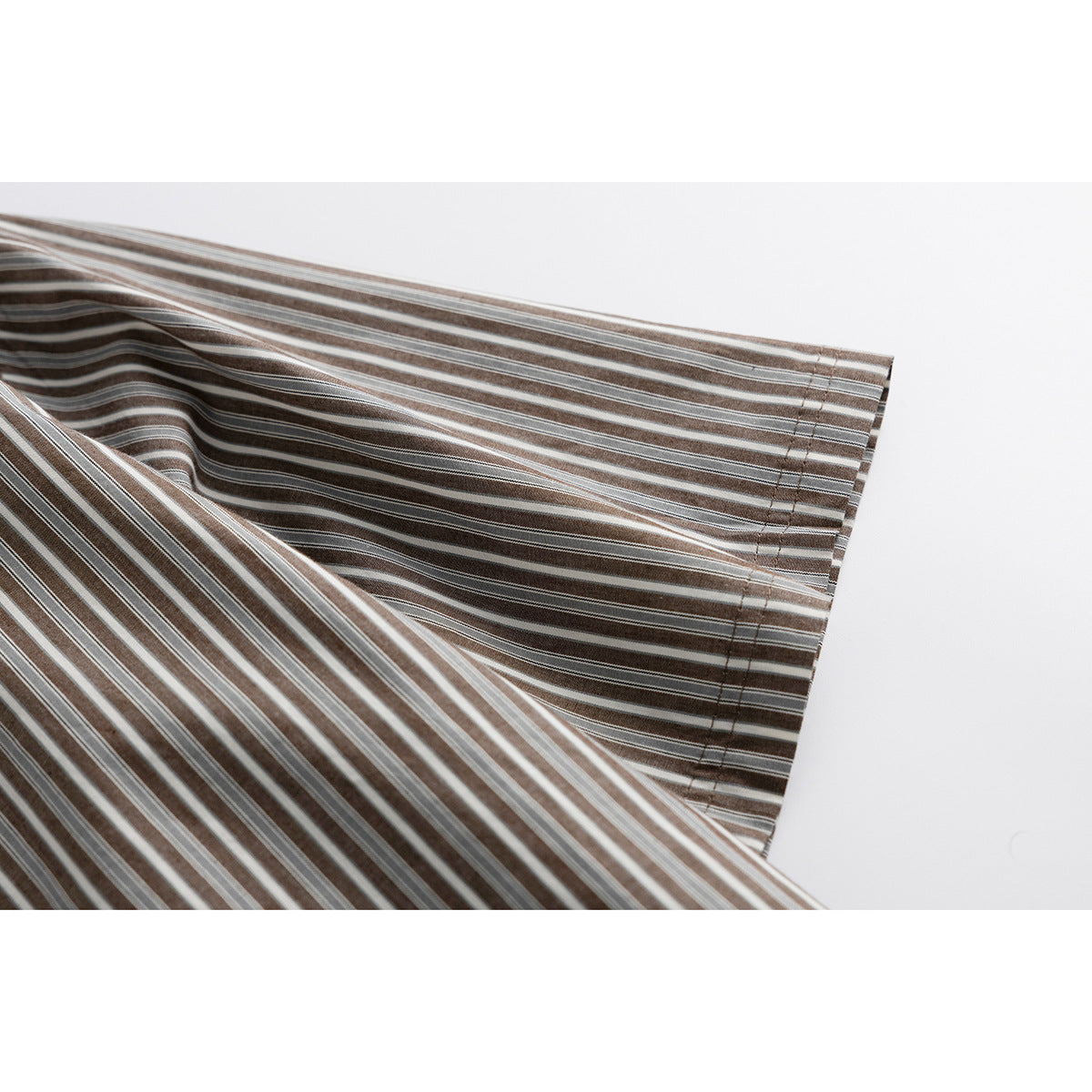Close-up of a short sleeve and stitched hem on the brown, gray and white striped shirt.