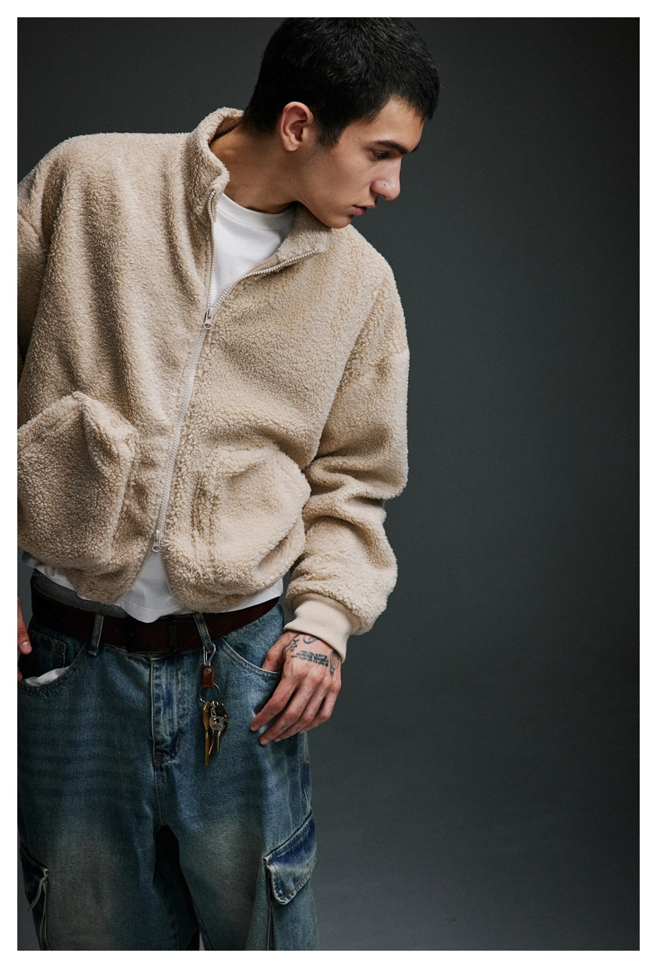 Angled view of a model wearing a beige zip-up fleece jacket with a stand collar and large front pockets.