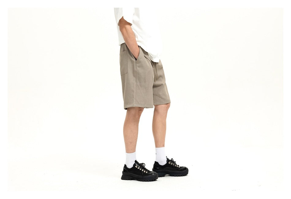 Side view of a cropped model wearing light taupe shorts with an elastic drawstring waist and side pockets.