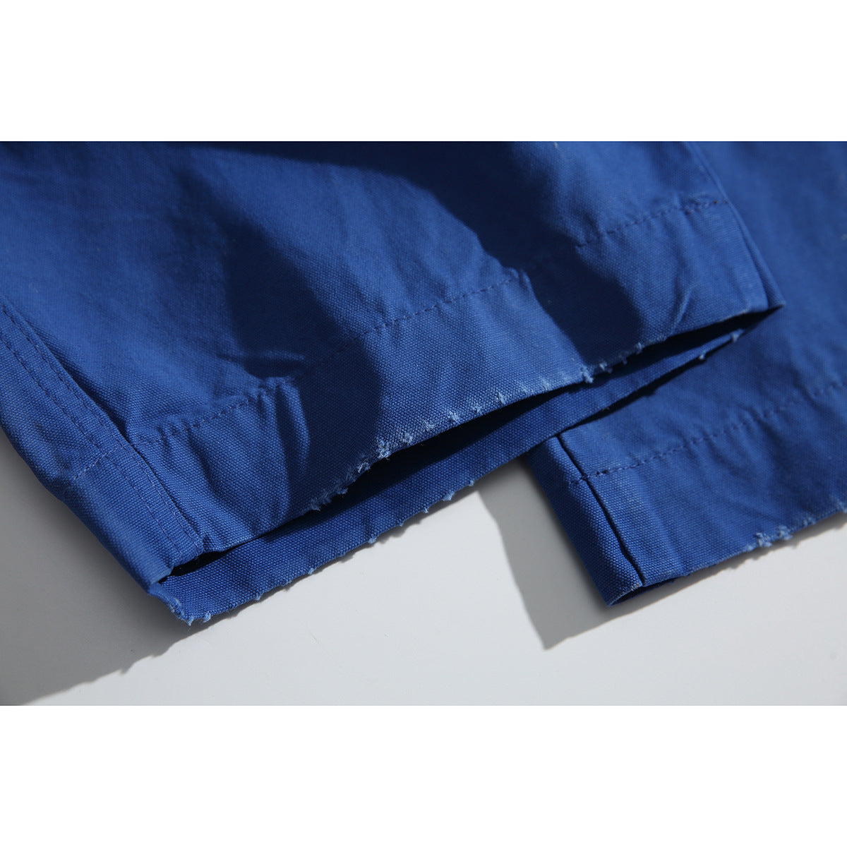 Close-up of the stitched hem on cobalt-blue trousers, showing the fabric texture and seam.