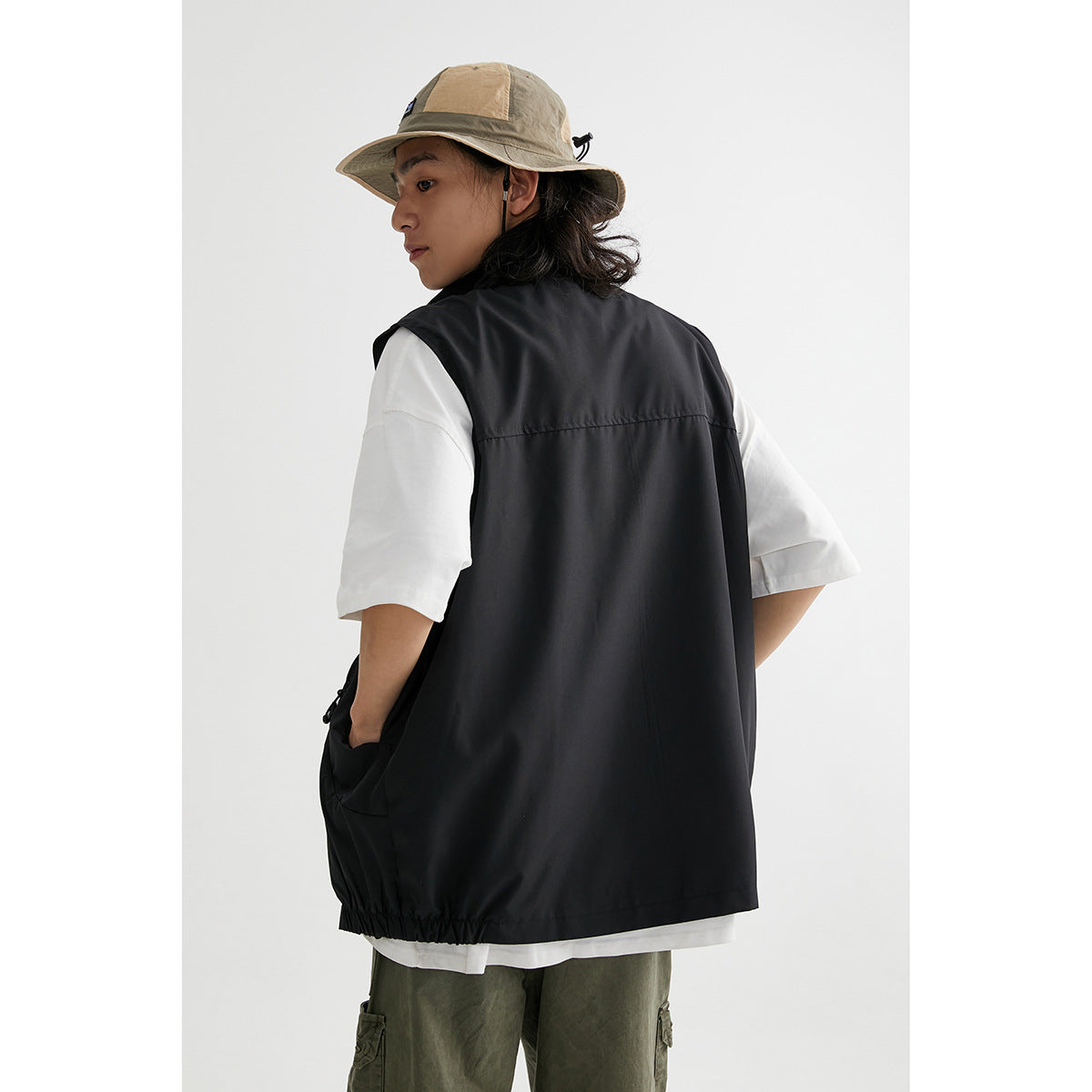Rear view of a model wearing a long black sleeveless vest over a white T-shirt.