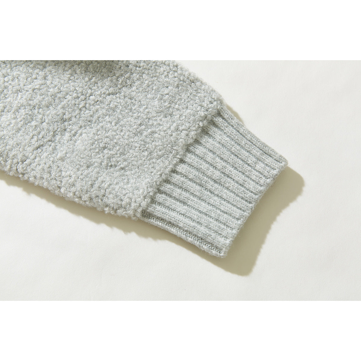 Close-up of a light gray cardigan sleeve with a wide ribbed cuff and textured knit.