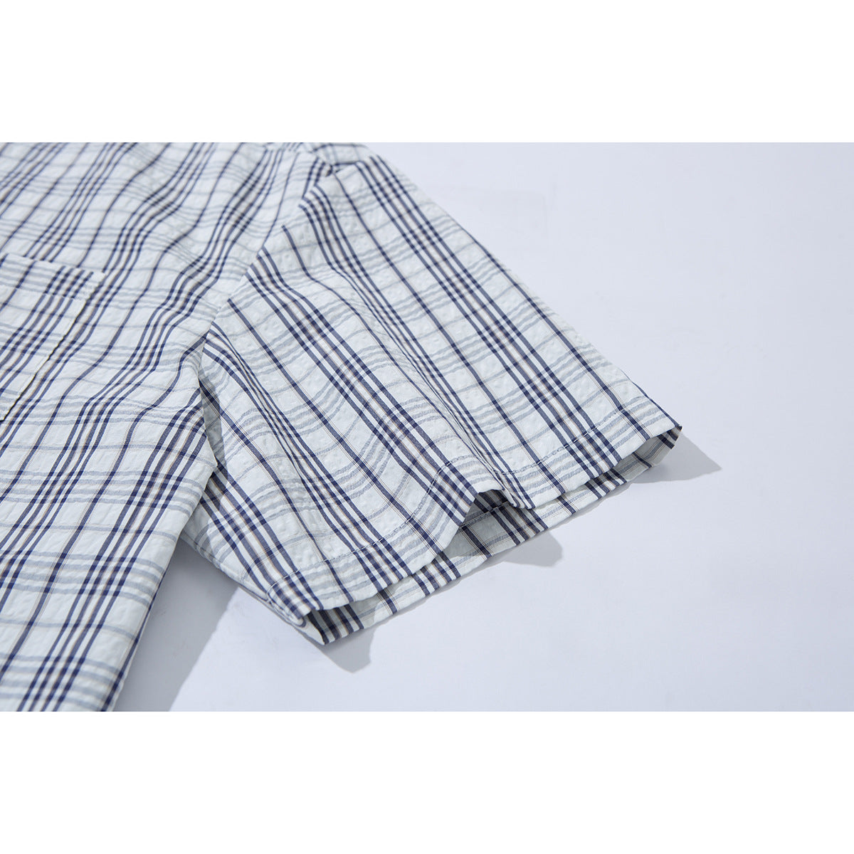 Close-up of the short sleeve and hem on a white shirt with blue-gray plaid.