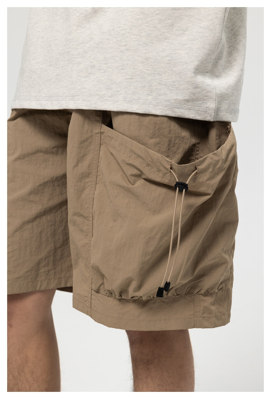 Close-up of a person wearing taupe shorts with a large side cargo pocket and adjustable drawcord.