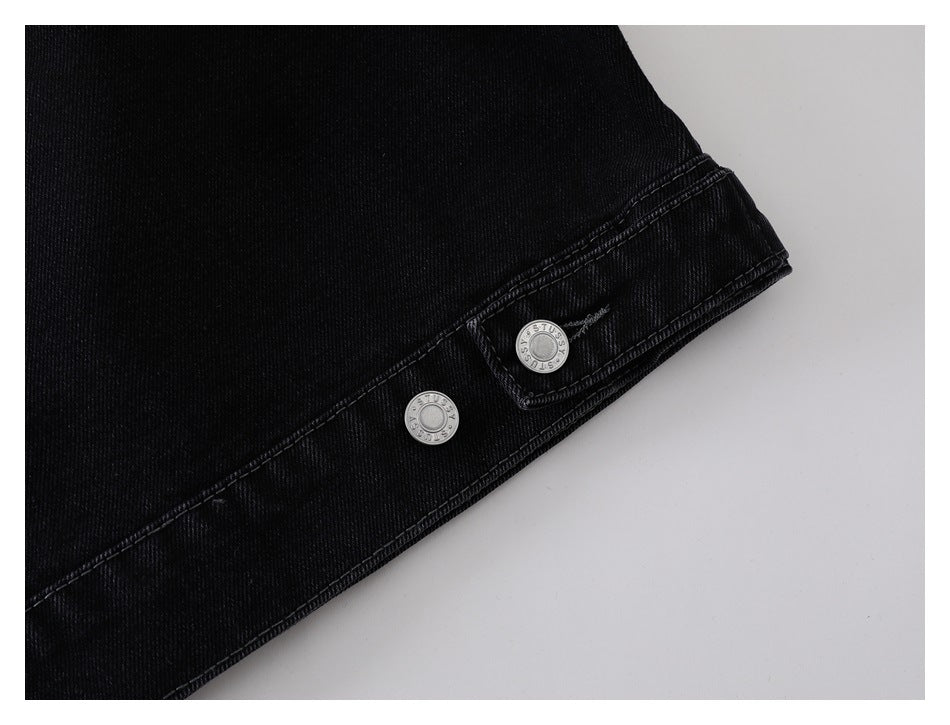 Close-up of a black denim jacket cuff with two silver snap buttons.