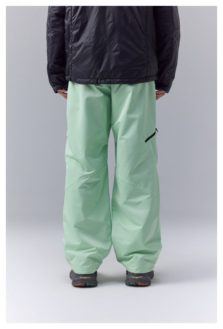 Back view of mint-green loose-fit pants with a black zip pocket, worn with a black jacket.