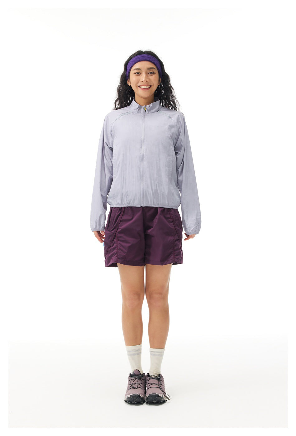 Model wearing a light lavender zip-up jacket, plum shorts, white socks and trail shoes, shown facing forward.