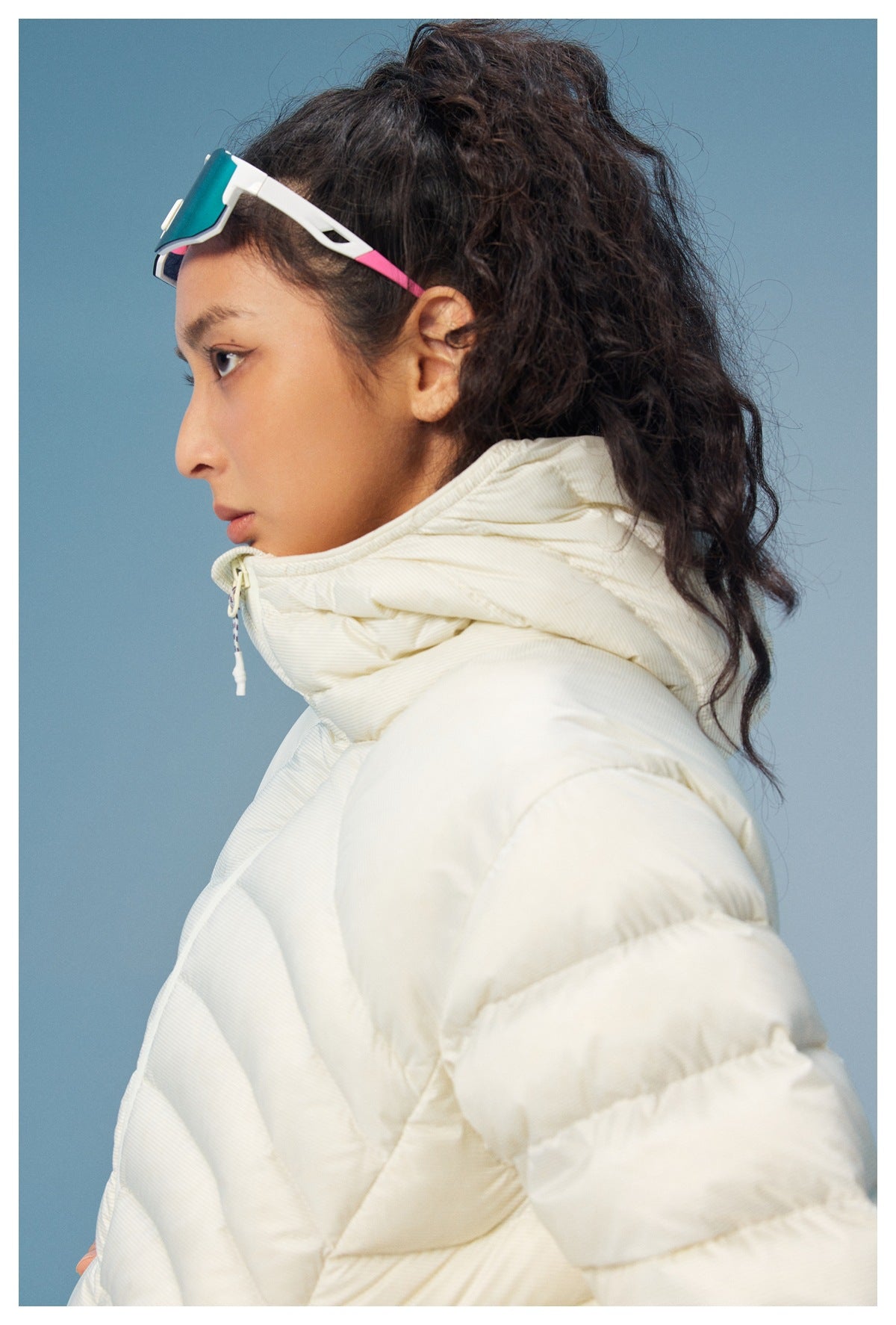Side profile of a model wearing a cream puffer jacket with a tall gathered collar and front zipper.