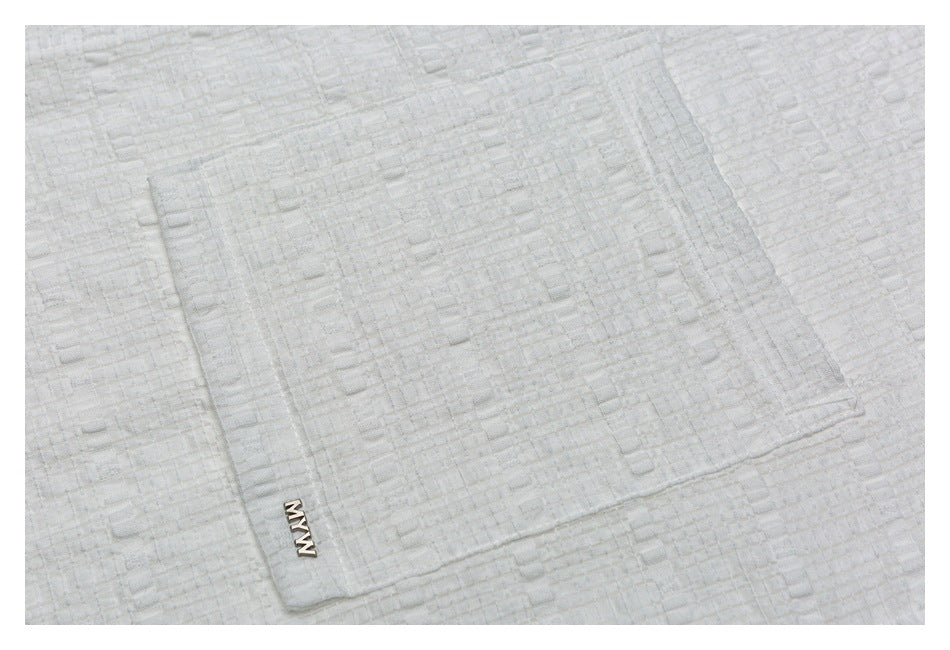 Close-up of the white shirt's textured fabric and small logo on its pocket.