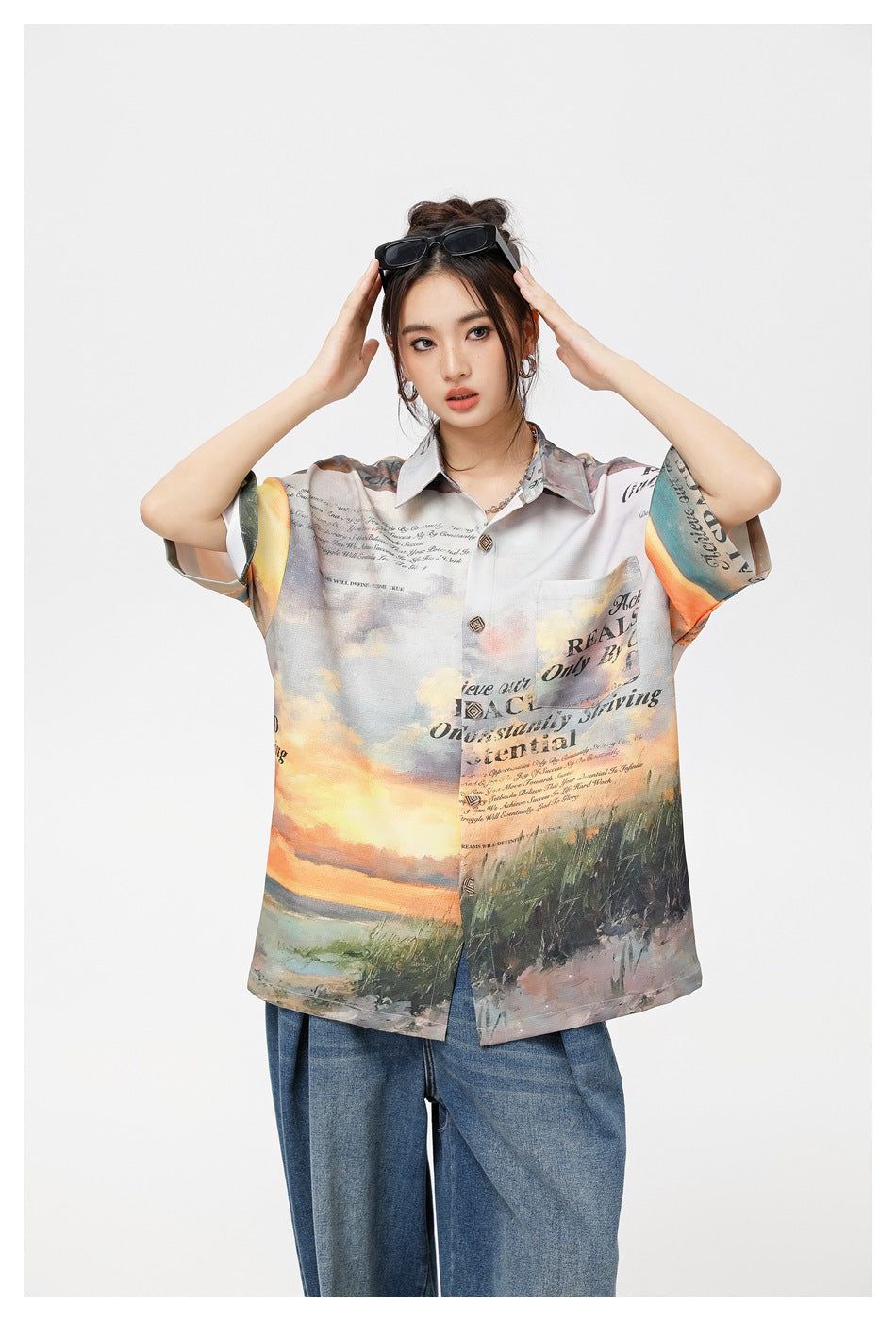 Front view of a model wearing an oversized sunset-print shirt with a pointed collar, chest pocket and short sleeves.