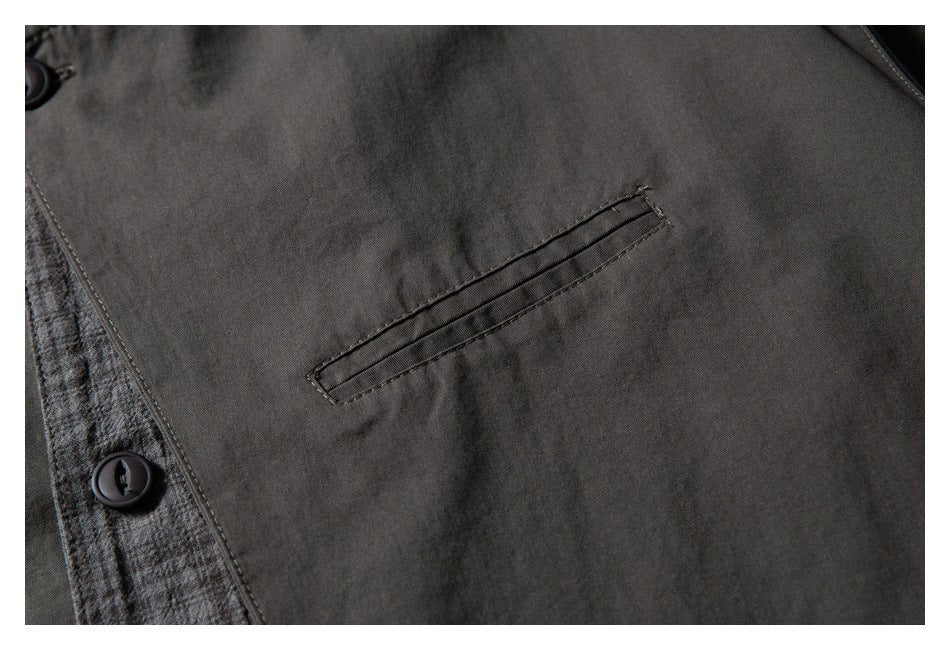 Close-up of a narrow welt pocket on dark charcoal fabric beside gray plaid trim and buttons.