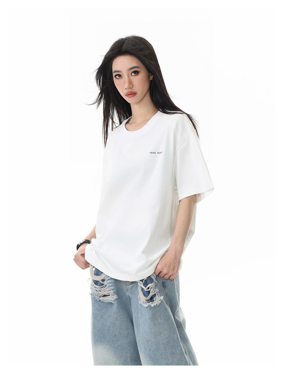Model wearing white loose short-sleeve T-shirt with small chest text print and light-blue distressed jeans, angled view