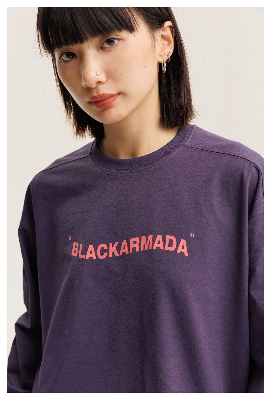 Close-up of the plum T-shirt's ribbed crew neck, coral BLACKARMADA chest print, and shoulder seams on a model.