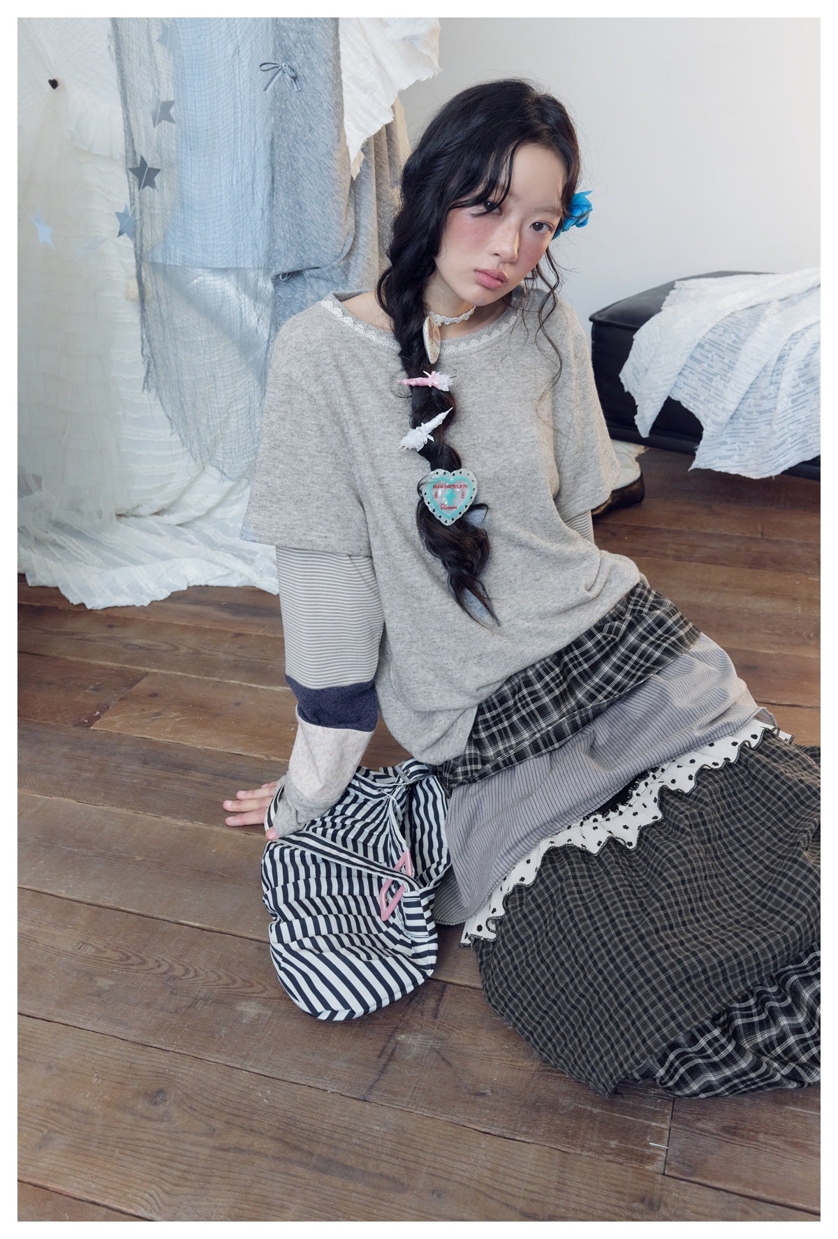 Model seated on a wood floor in the gray top with lace neckline, striped sleeve layer and navy and floral sleeve blocks