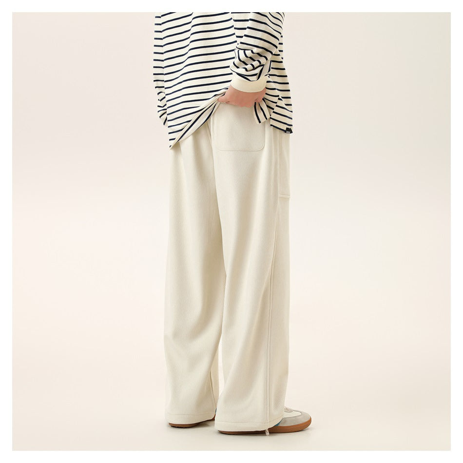 Rear view of a model wearing wide-leg ivory ribbed pants with a patch pocket and ankle zips.