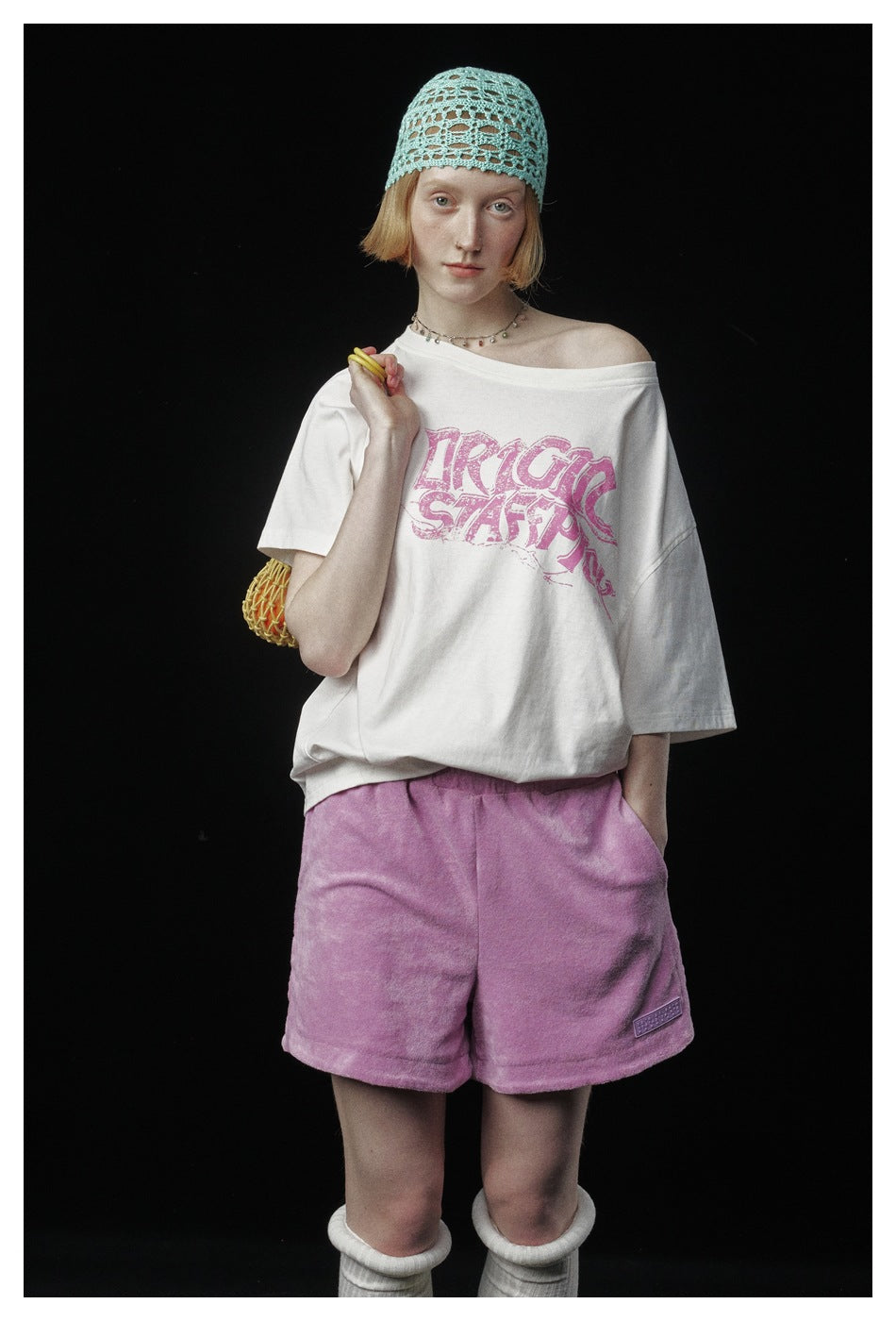 Front view of a model wearing an off-white pink-graphic T-shirt and pink shorts, with a turquoise open-knit cap.