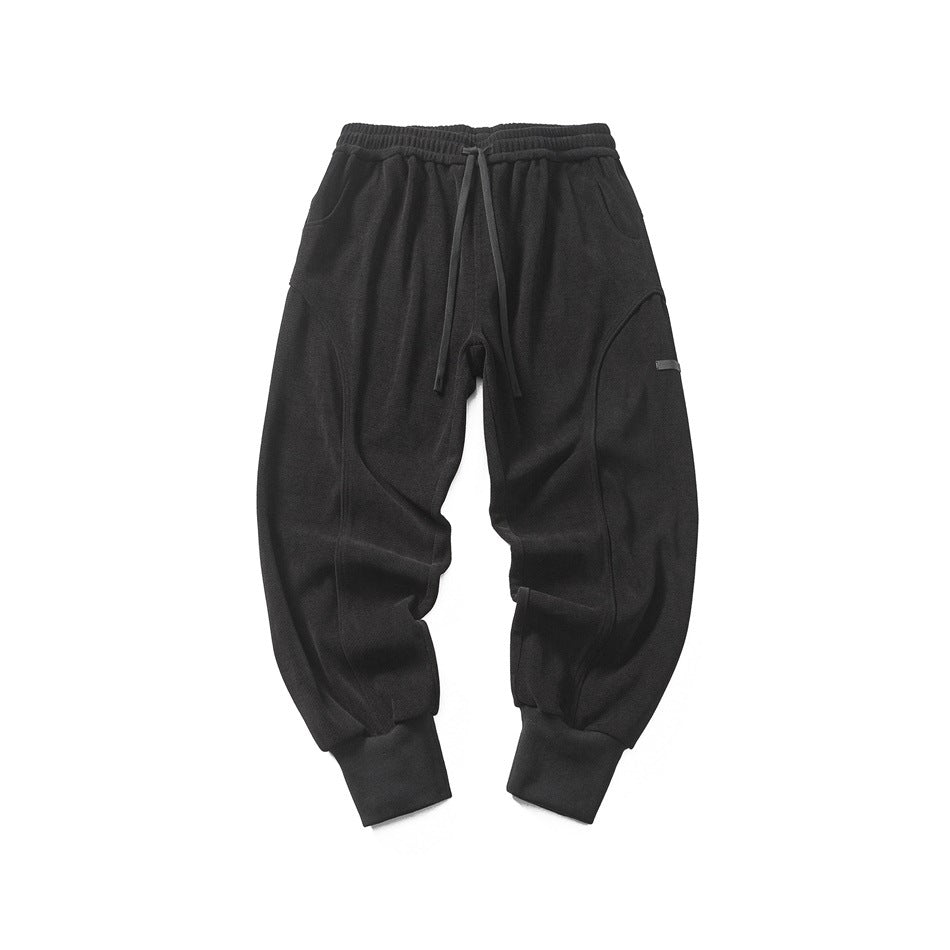 Black drawstring jogger pants with curved leg seams and ribbed cuffs, front flat lay