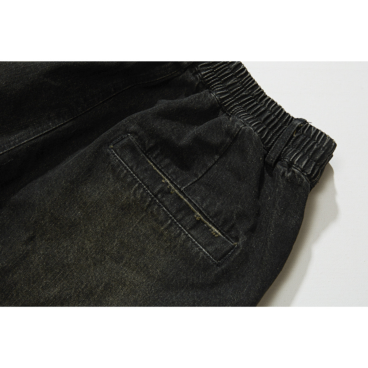 Close-up of black denim shorts showing a slanted pocket and gathered elastic waistband.