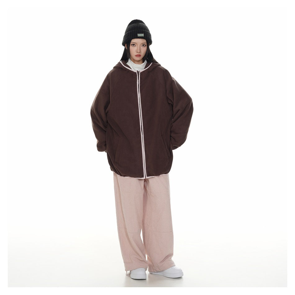 Model wearing an oversized dark brown zip-up hoodie with white trim and pale pink loose trousers.
