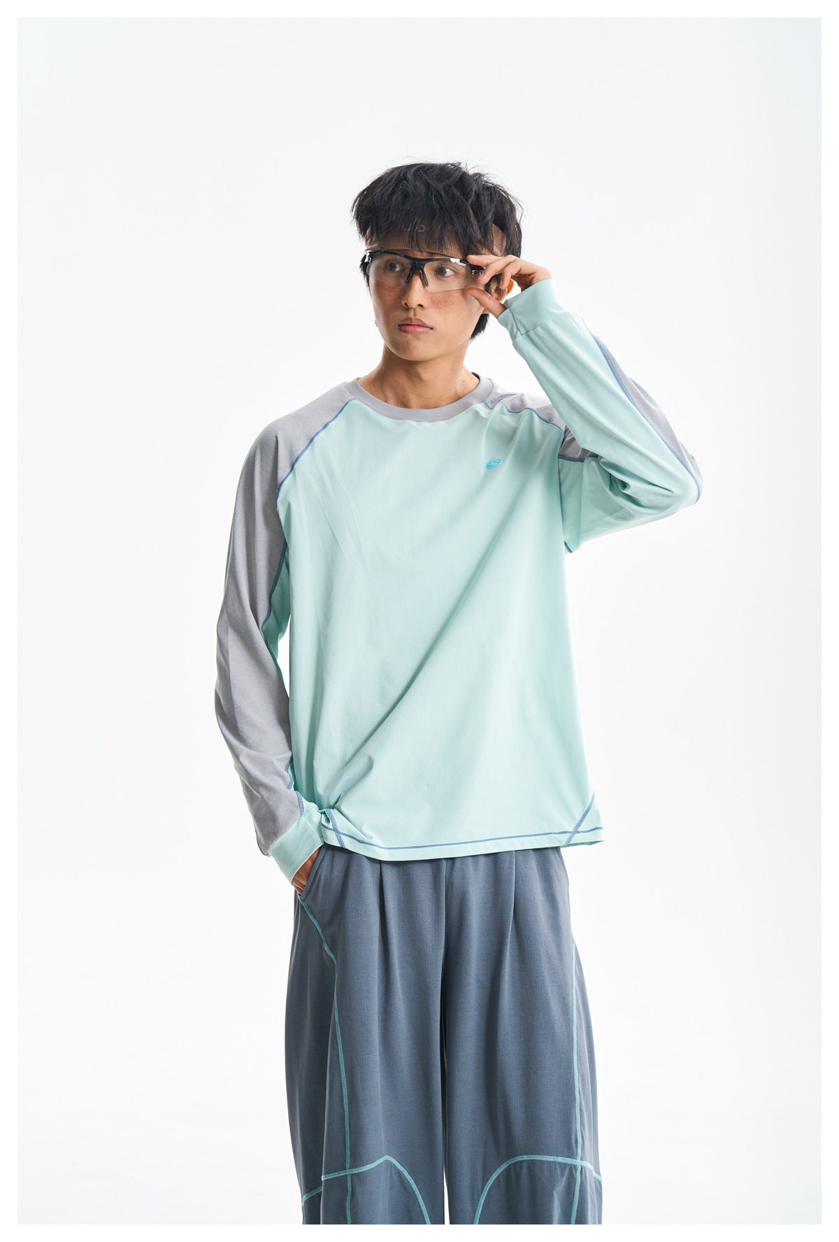Front view of a model wearing a mint-green long-sleeve shirt with gray sleeves and loose slate-blue trousers.