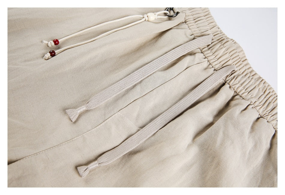 Close-up of beige pants showing the elastic waistband, front pocket seams, and two drawstrings.