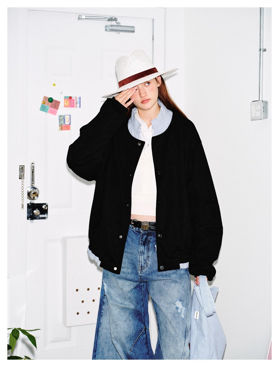 Model wearing a black snap-front jacket with a round neck and roomy sleeves, styled with a white hat and blue jeans.