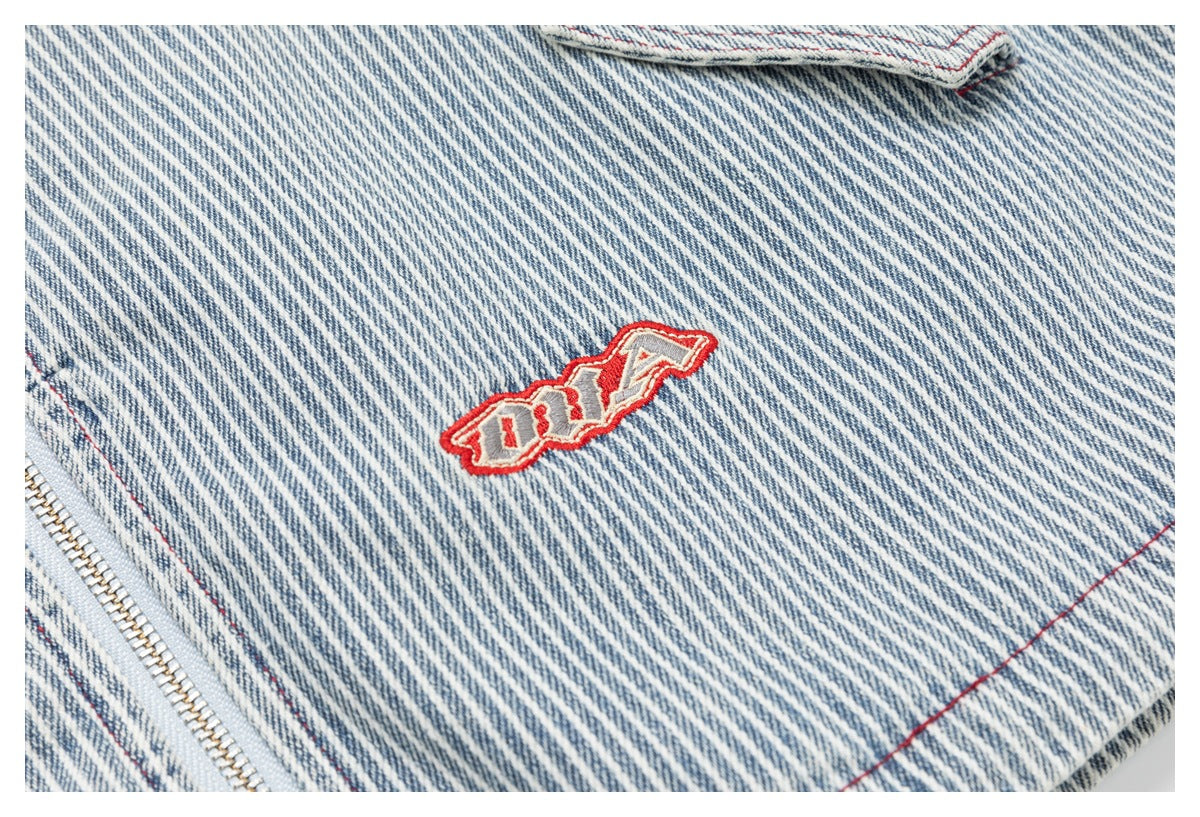 Blue-and-white striped garment detail with a small red-and-white embroidered patch beside a metal zipper.