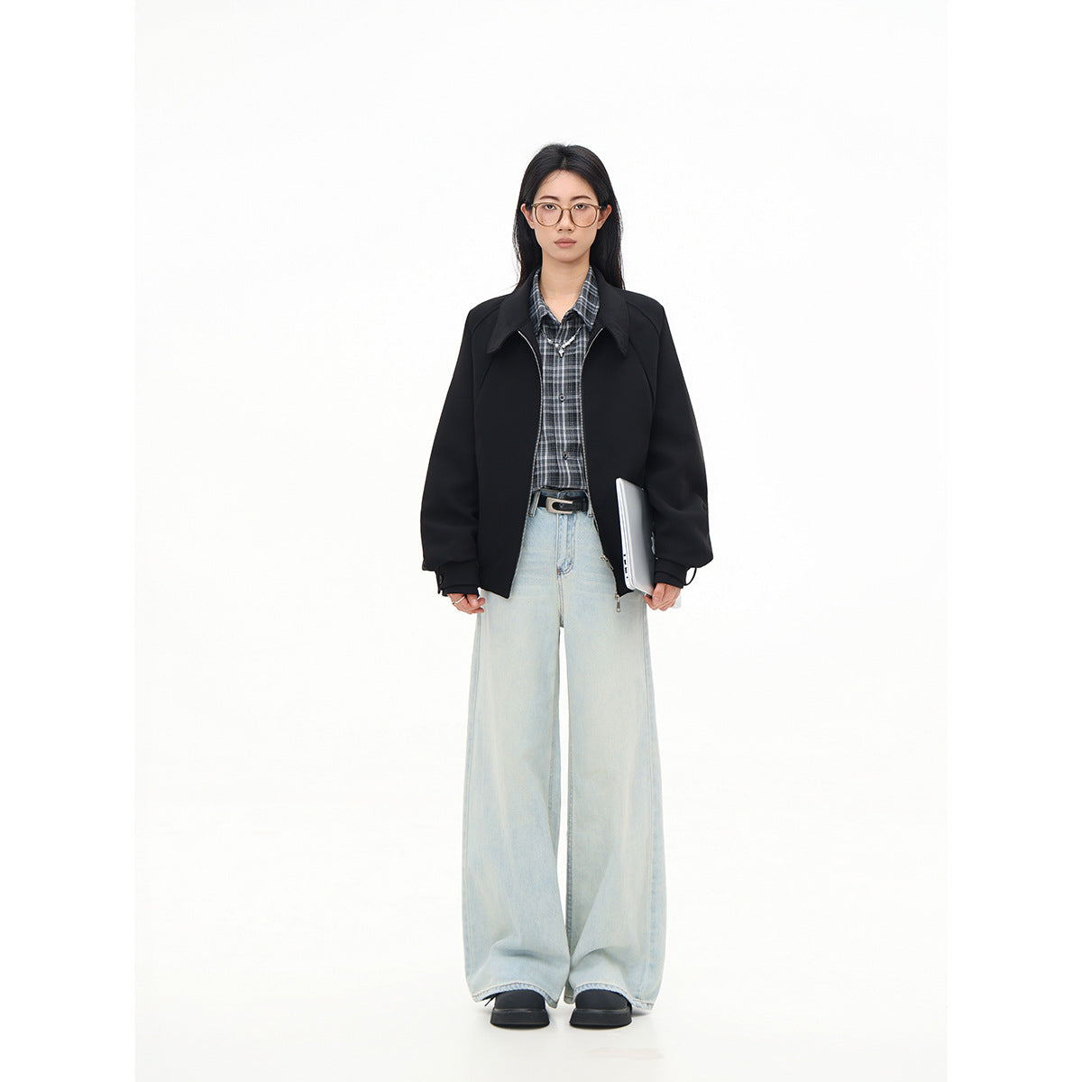 Full-length front view of a model wearing a black jacket, gray plaid shirt, and pale wide-leg jeans.