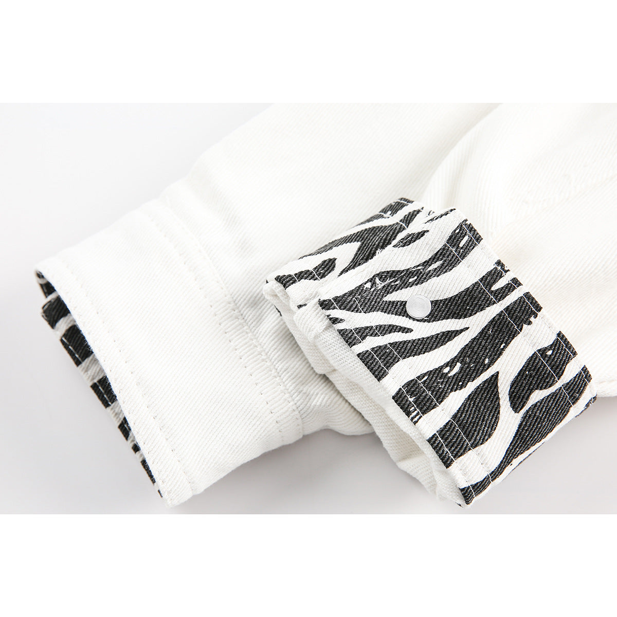 Close-up of a white jacket cuff with a black-and-white patterned tab and snap button.